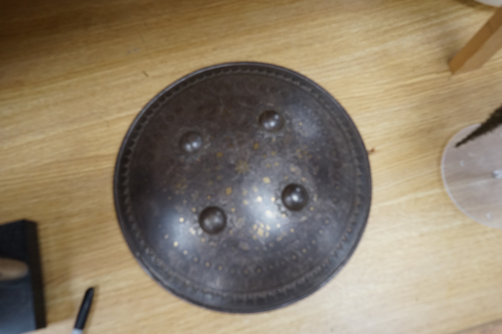 A mid to late 19th century Indian helmet and matching shield, covered with silver koftgari decoration, the helmet with sliding nasal bar and twin plume sockets surmounted by a third plume socket, the skull fluted like a